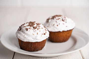 Cupcakes with whipped cream and chocolate chips on a white plate on a white wooden table. Image for the menu or catalog of confectionery products.