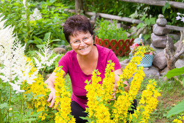 Positive middle-aged woman sitting among flowers in a beautiful summer garden