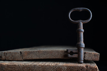 three old rusty keys stand on old wooden board against a dark background