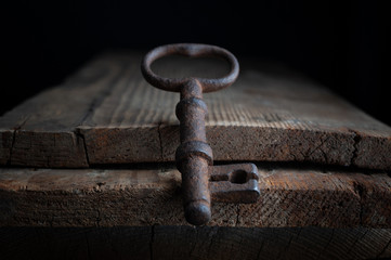 three old rusty keys stand on old wooden board against a dark background
