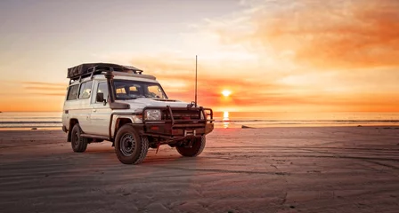 Zelfklevend Fotobehang Ontspannend avontuur in de outback met 4WD-voertuig op het strand van een oceaan bij zonsopgang © HLPhoto