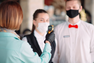 The Manager of a restaurant or hotel checks the body temperature of the staff with a thermal...