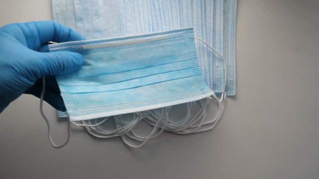 A man takes a medical mask. A man s hand in a blue sterile glove pulls out a disposable mask from a pile and puts it on his face.