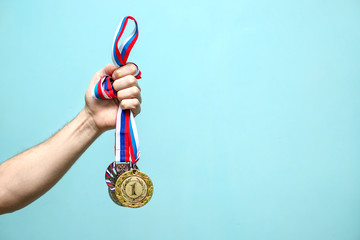 the male hand of the winning athlete holds the highest-ranking medals on a blue background space...