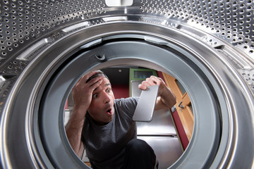 Worried caucasian man taking out a phone from the drum of the washing machine. Interior view.