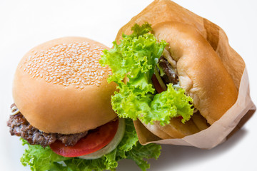 Closeup top view two hamburger made from pork or beef, green lettuce bread onion white sesame and tomato in a paper bag on a white table background made at home. Burger is delicious American fast food