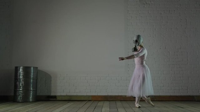 A ballerina in a gas mask performs dance movements against the background of an oil barrel.