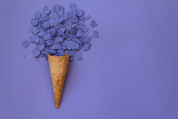 Top view of ice cream cone with purple confetti on purple background with copy space