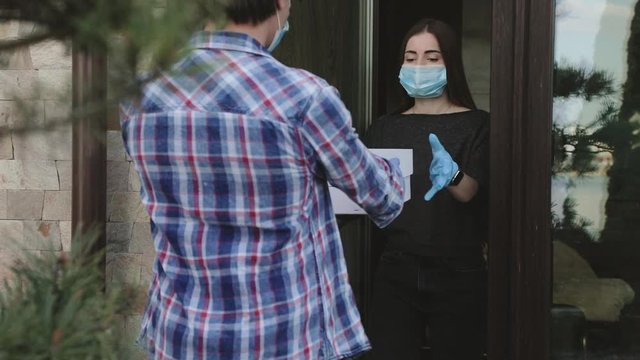 Isolated girl in mask receiving safe delivery of order at home entrance