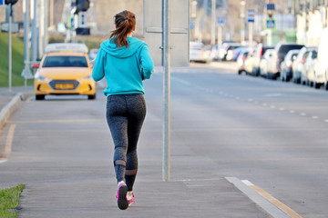Slim girl running on the sidewalk along the city street, rear view. Alone runner, concept of workout, slimming in spring season