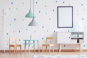 Mockup poster in black frame, pastel colored lamps and wooden furniture in bright kid's playroom interior