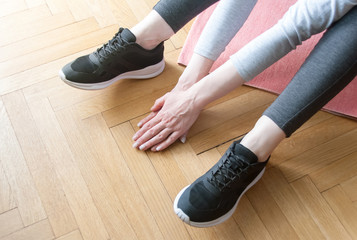 Young woman in sports wear doing stretching at loft studio on sport mat. Legs and hands close up. Workout and healthy life concept
