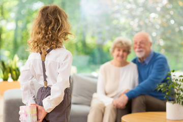 Cute blond child standing with gift behind her back on the grandparent's day