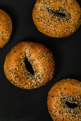 Freshly Baked Bagels Topped with Sesame Seeds, Poppyseeds, Garlic and Onion on Black Background. Selective focus.