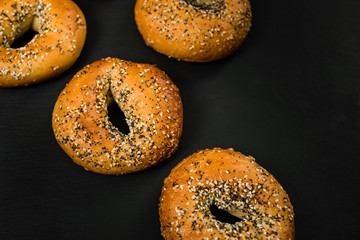 Freshly Baked Bagels Topped with Sesame Seeds, Poppyseeds, Garlic and Onion on Black Background. Selective focus.
