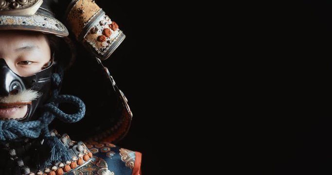Japanese man in traditional samurai armor and authentic helmet looking at camera, isolated on black background - close up portrait shot 4k footage