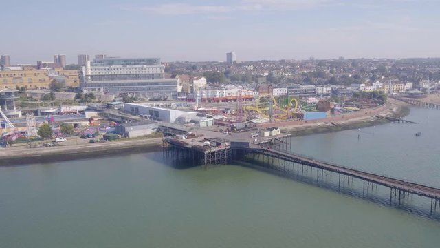 Drone or aerial pan of Southend pier and funfair showing the sea, promenade and beach with hotels, rollercoaster, shops and arcades