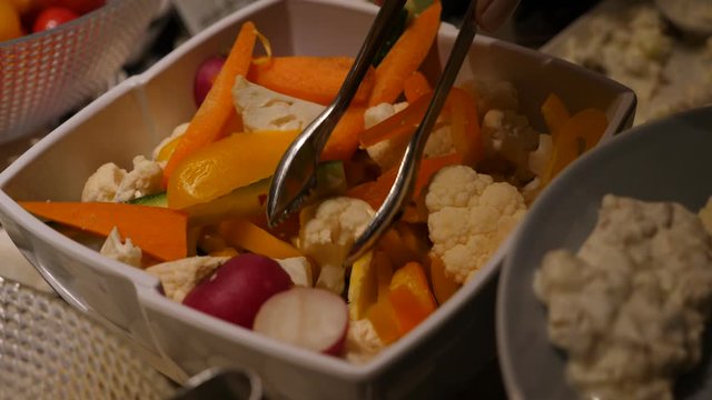 Woman using tongs and pick up only white curds of cauliflower from salad bowl, closeup shot. Fresh and healthy vegetables at breakfast buffet table, self service