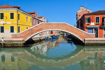 Fototapeta na wymiar Picturesque Venetian canals with bright colorful buidlings and bridge on the blue sky background