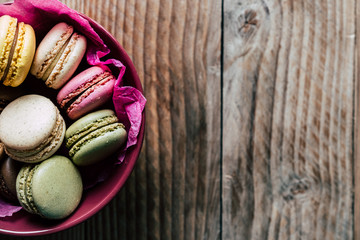 Macarons colorés dans un bol rose sur un fond en bois
