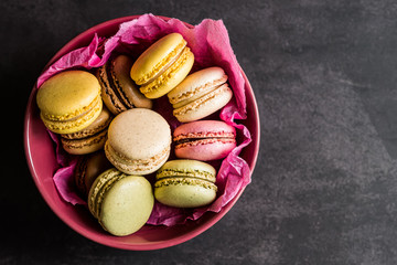 Macarons colorés dans un bol rose sur un fond noir
