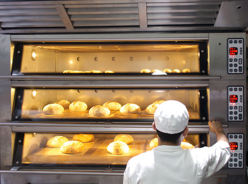 Male baker putting bread into the oven