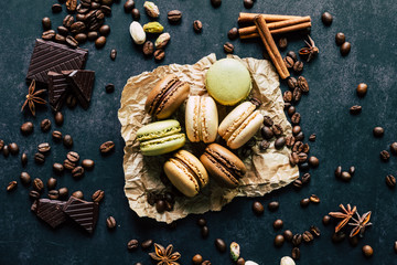Macarons saveur vanille chocolat pistache et café avec des morceaux de chocolat des pistaches des batons de cannelle et des pistaches sur le fond noir