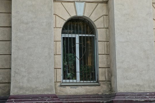 one white window behind the iron bars on the brown old concrete wall of the building