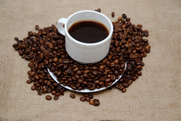 coffee beans sprinkled on a white saucer from above a cup with coffee.