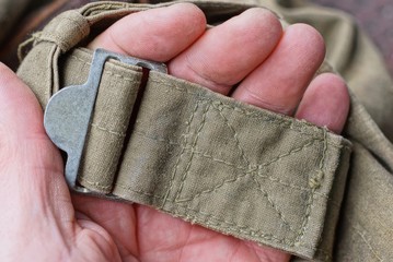 Obraz premium fingers hold a gray iron carbine on an old green harness made of fabric on a backpack