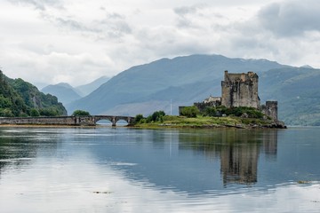 Fototapeta na wymiar Reflection of Eilean Donan Castle, Scotland and the bridge in waters of Loch Duich in typical Scottish cloudy weather