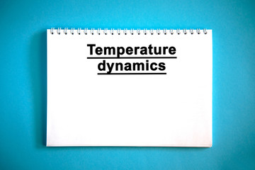 Temperature dynamics - text on a white notebook on a blue background