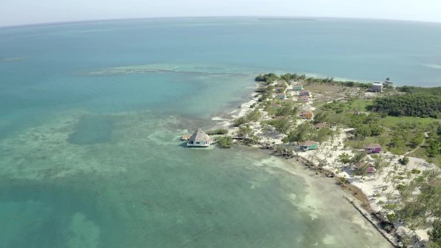 Aerial shot of sea with houses and trees on shore during sunny day, drone moving over beach against sky - Coco Plum Cay, Belize