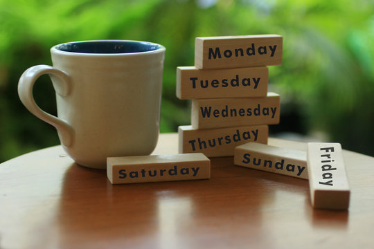 A white coffee cup and the names of the day written on wooden blocks - Sunday, Monday, Tuesday, Wednesday, Thursday, Friday, Saturday. Today or weekly plans and goals concept.
