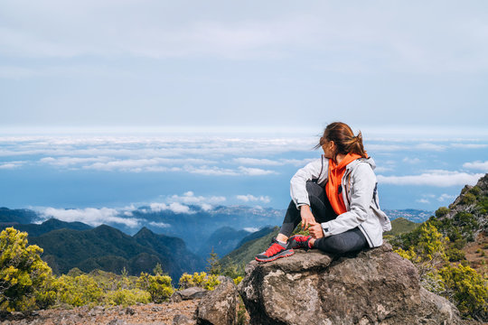Young adult caucasian female dressed  sporty clothes resting on the rock and enjoying clouds view from Pico Ruivo mount 1861m - the highest peak on the Madeira Island,Portugal. Active vacation concept