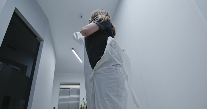 Woman getting dressed in full protective PPE suit or clothing during the Covid-19 coronavirus pandemic in a low angle view in a white corridor - slow motion