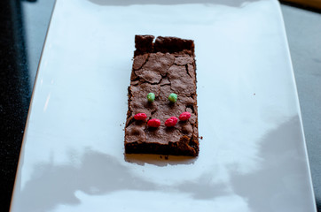 Homemade brownie on white plate. Brownie on black counter. Brownie with decoration. Brownie with smiley.
