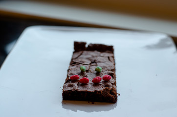 Homemade brownie on white plate. Brownie on black counter. Brownie with decoration. Brownie with smiley.