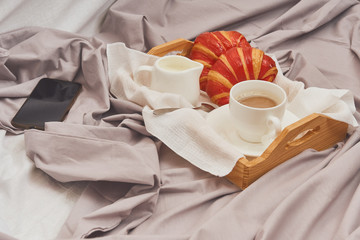 Fototapeta na wymiar Breakfast on a crumpled bed, coffee, croissants, mobile phone
