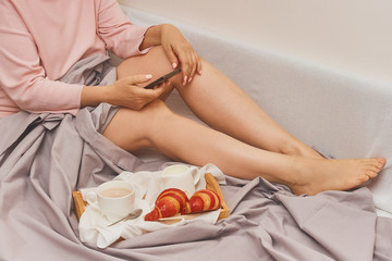Woman in bed with breakfast typing a message in a mobile phone