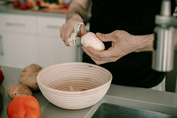Food preparation. Peeling potatoes. Potato skin. Kitchen counter. Kitchen sink. Making dinner. Man cooks dinner. Husband helps to cook dinner. Peeler utensil. Lifestyle kitchen. Food waste. Vegetable