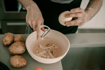 Food preparation. Peeling potatoes. Potato skin. Kitchen counter. Kitchen sink. Making dinner. Man cooks dinner. Husband helps to cook dinner. Peeler utensil. Lifestyle kitchen. Food waste. Vegetable