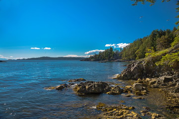 Fototapeta na wymiar Vancouver Canada, Strait of Georgia, Bowen Island, rocky shore of northern sea and wooded islands against the background of mountain range and blue cloudy sky 