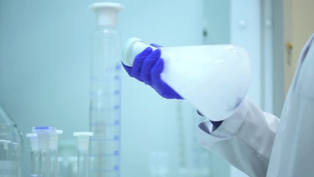 chemist in chemical laboratory holding a flask transparent liquid reagent and shaking it Spbd. measuring cylinders, beakers in lab. bubbles ib glass. concept research, checking, reaction