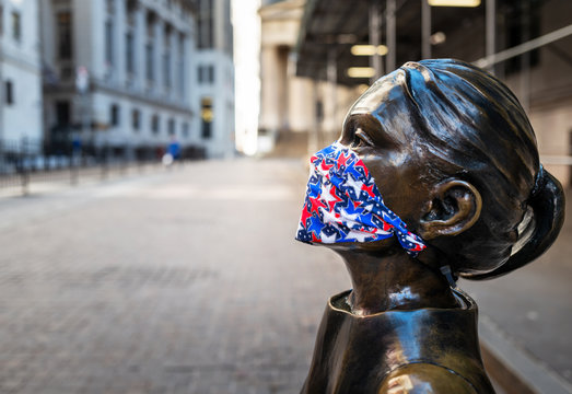 Fearless Girl Statue Wearing Face Mask  In Front Of New York Stock Exchange Representing The Covid-19 Pandemic Face Mask Requirements During NYC Lockdown.