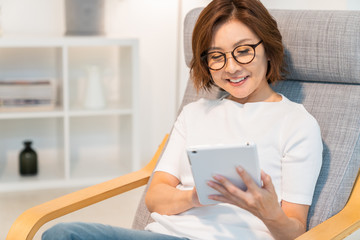 部屋でタブレットを見るシニア女性