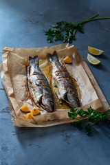Two baked sea Bass fish or lavrak or sea wolf on baking paper on a baking sheet. Top view, horizontal. Menu or recipe book concept