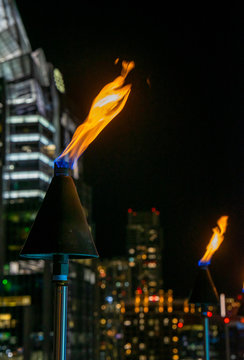 A Closeup Of Fire Torches Overlooking The Evening Landscape Of Austin, Texas From A Rooftop Bar