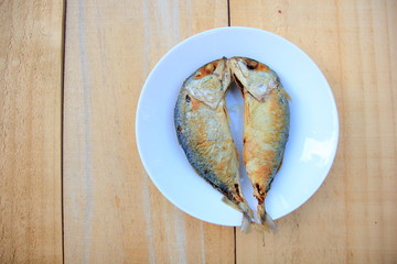 2 fried mackerel in a white plate on wooden background.
