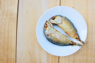 2 fried mackerel in a white plate on wooden background.